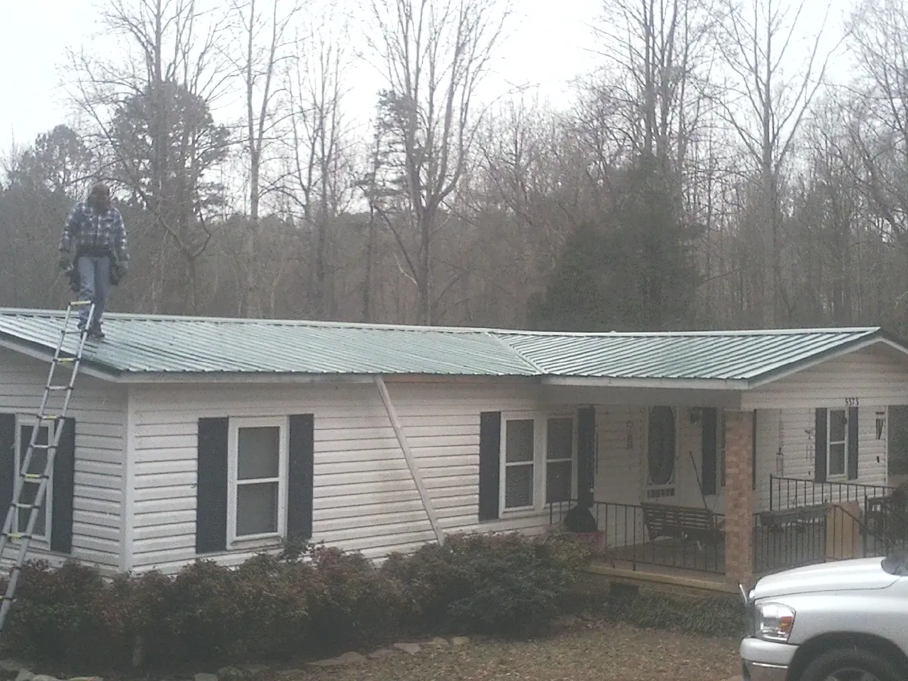 Worker on a ladder beside a new green metal roof on a ranch home in Childersburg
