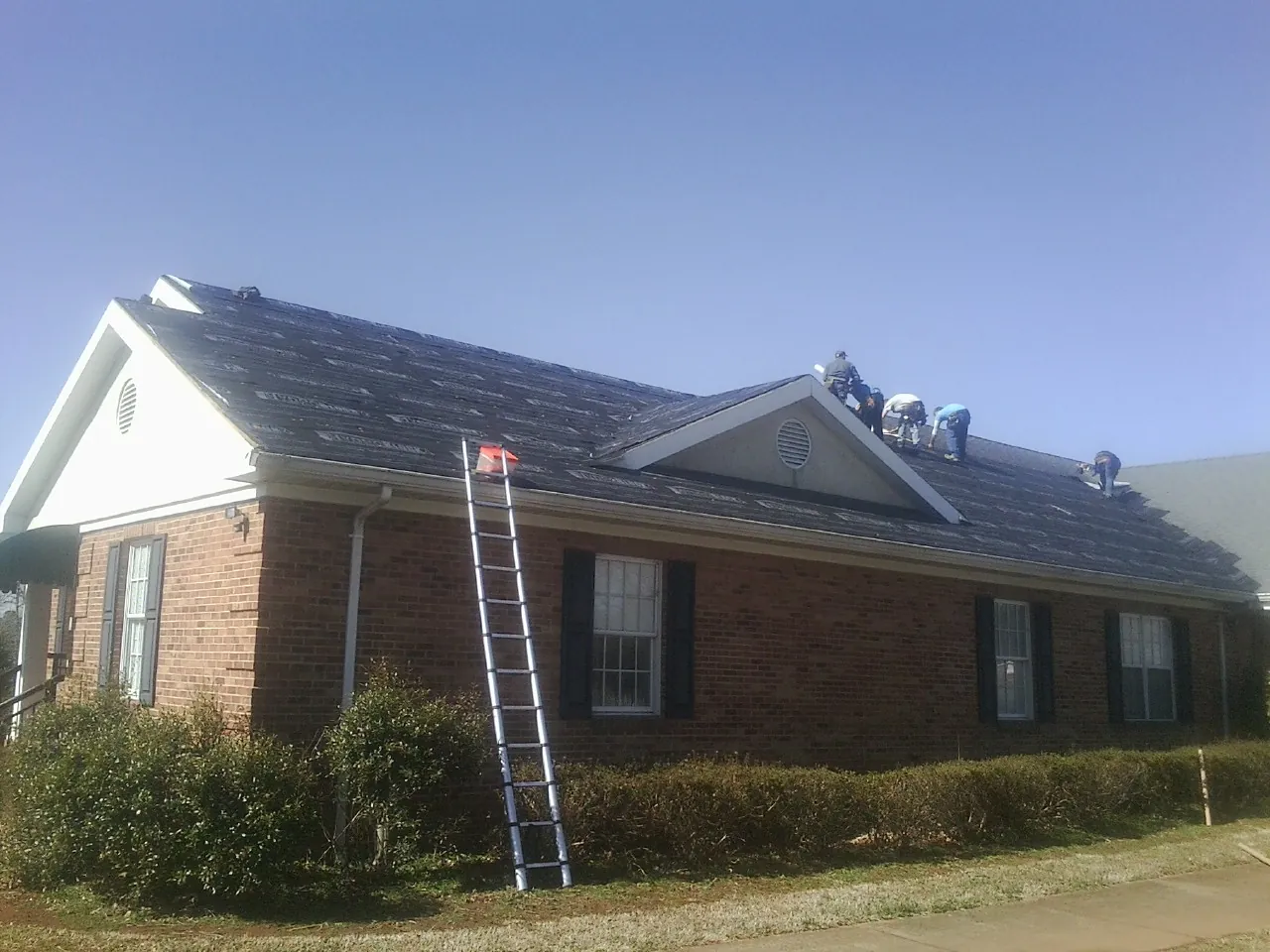 Crew tearing shingles off a brick ranch roof with a ladder set — Emergency Roof Repair work by our crew in Childersburg