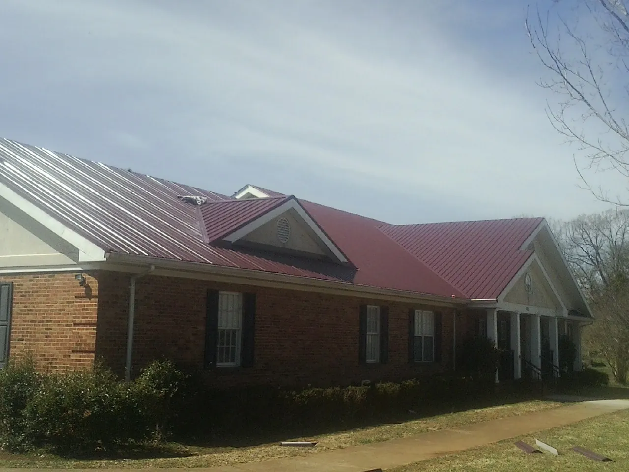 Red metal roof with gabled entries on a long brick building, from a Hail Damage Roof Repair job in Childersburg