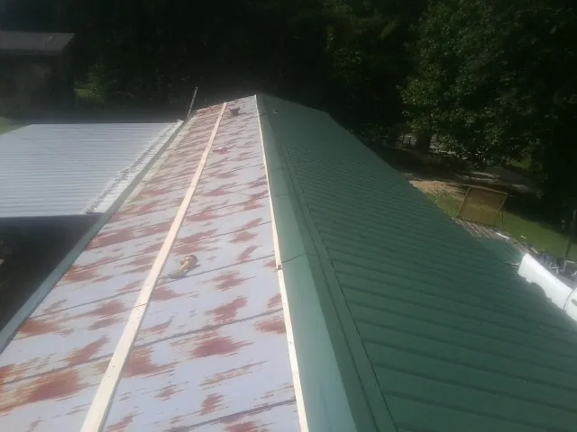 Old rusted panels beside newly installed green metal roofing — Wind Damage Roof Repair by Roofing Brothers in Childersburg