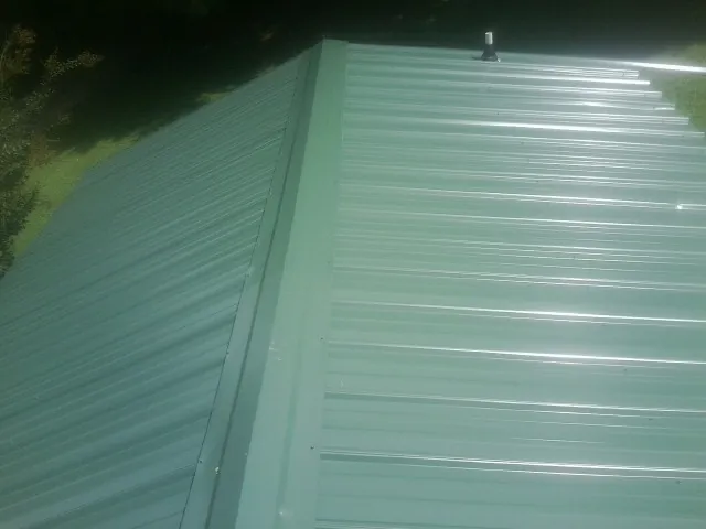 New green metal panels meeting at the ridge of a roof — Flat Roof Repair work by our crew in Childersburg