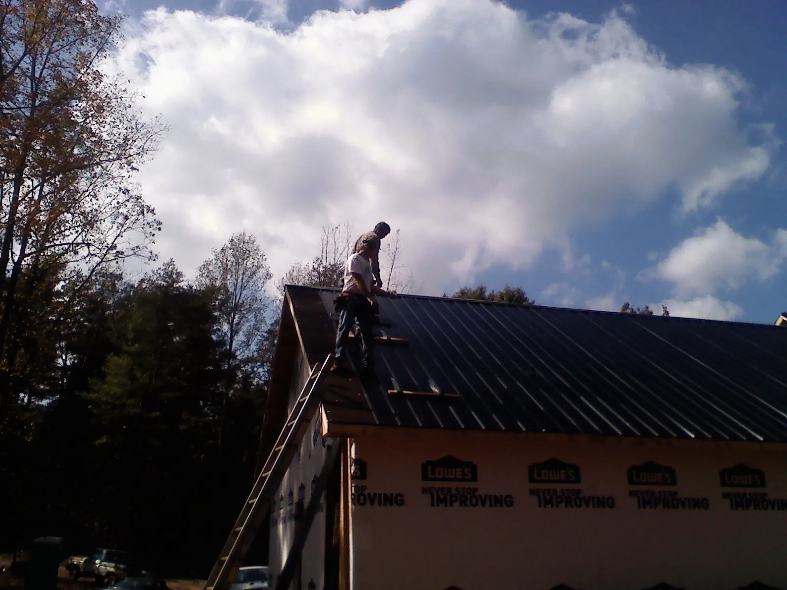 Roofer fastening dark metal panels high against a cloudy sky, from a Roof Inspection job in Childersburg