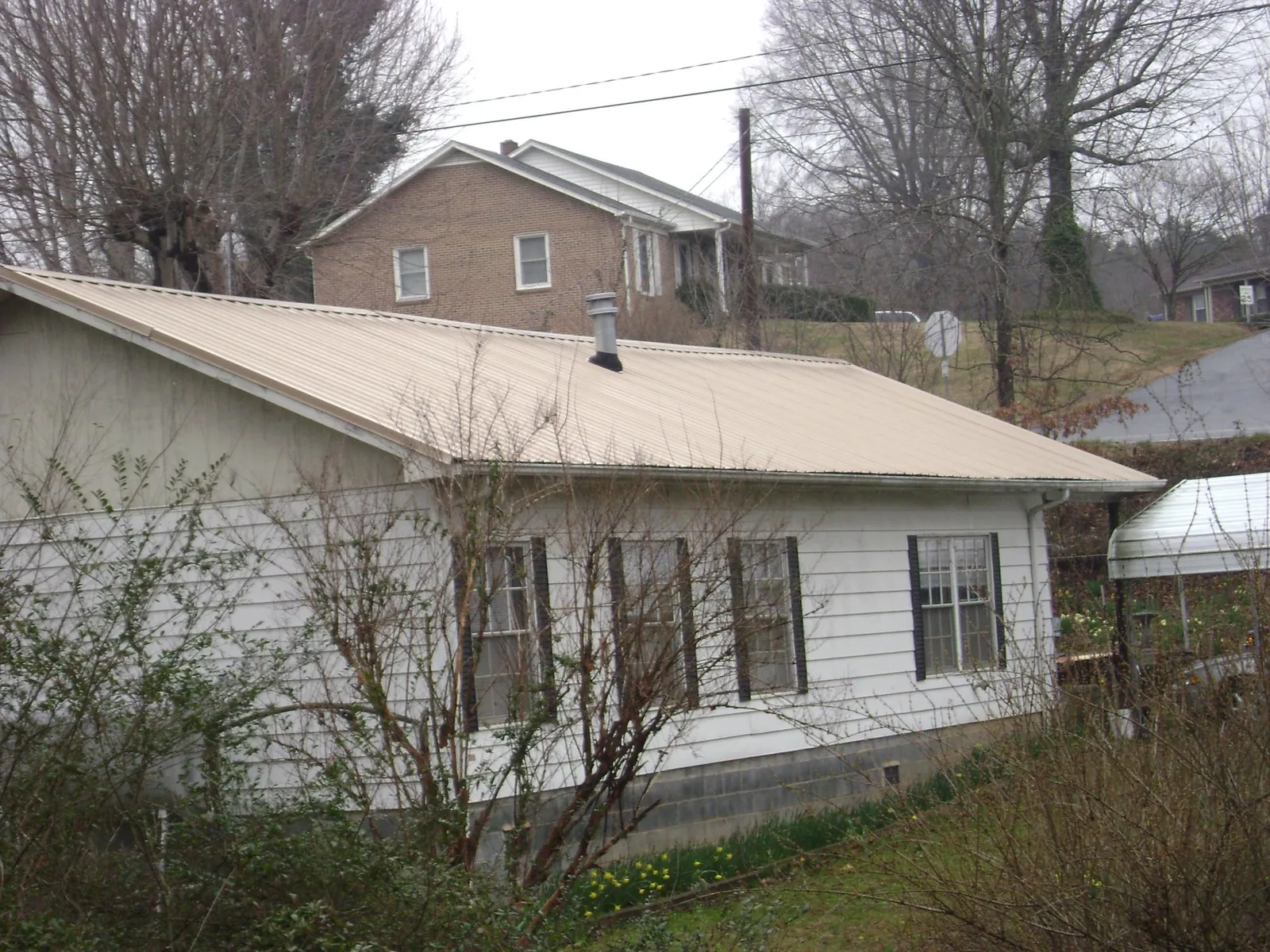 Tan metal roof on a white sided house set into a hillside — Commercial Roofing by Roofing Brothers in Childersburg