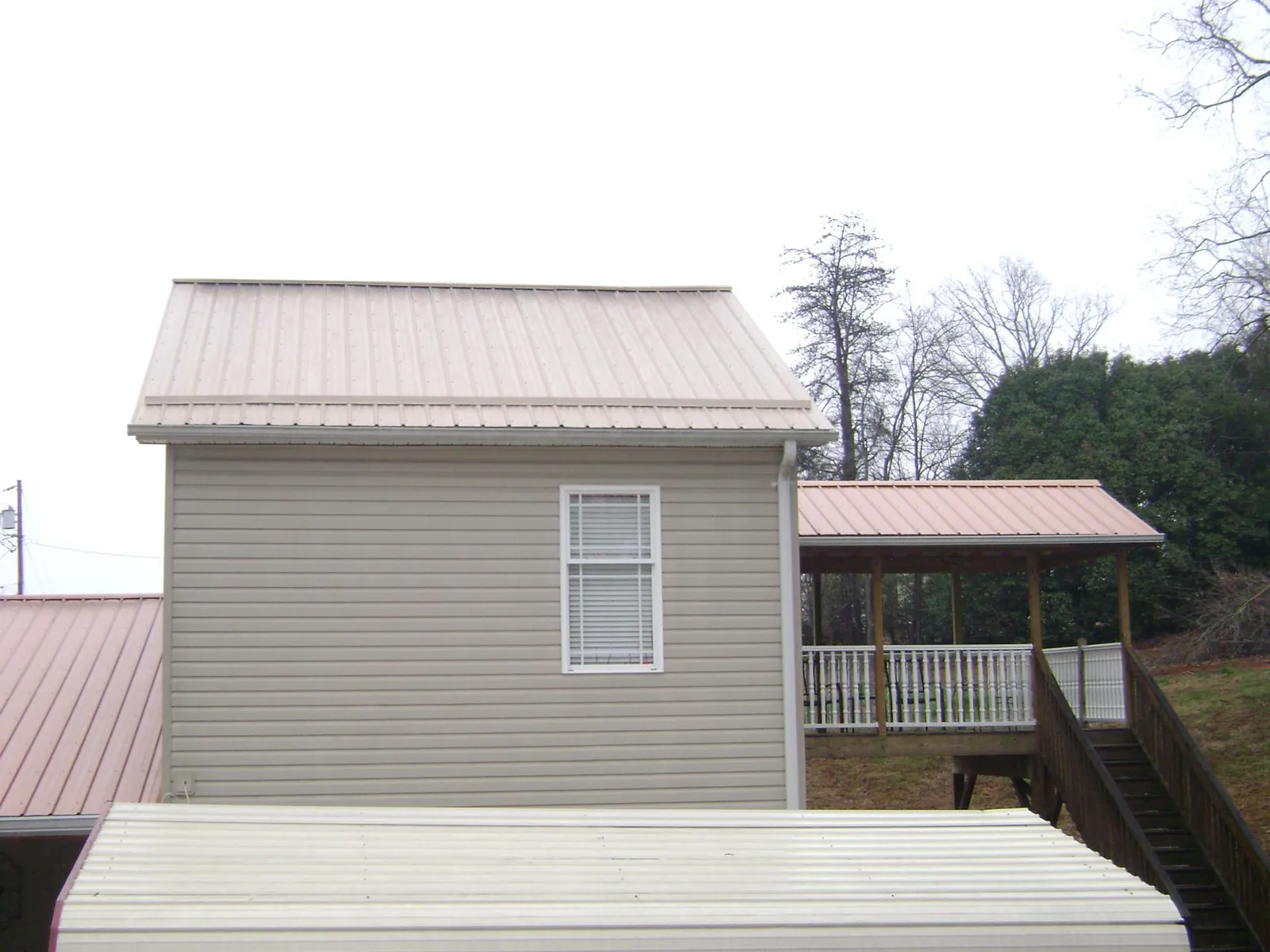 Tan metal roofs on a two story addition and attached porch, from a Roof Replacement job in Childersburg